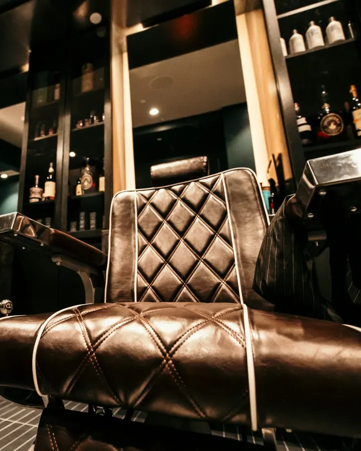 A quilted brown leather barber chair in a dimly lit barbershop